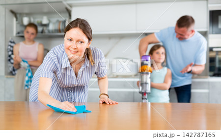 Woman rubbing table in kitchen while cleaning house with family Woman rubbing table in kitchen while cleaning house with family 142787165