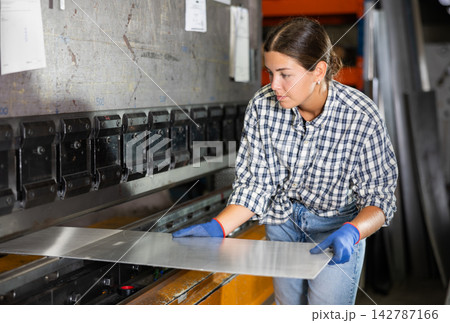 Young woman bends sheet of metal under pressure Young woman bends sheet of metal under pressure 142787166