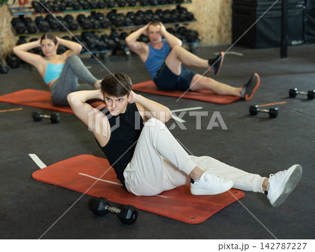 Motivated sporty young man lying on his back and training core muscles during group training class in CrossFit center 142787227