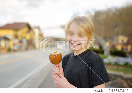 A charming preteen boy is eating a candy apple on the street of a small town Helen, Georgia, United States A charming preteen boy is eating a candy apple on the street of a small town Helen, Georgia, United States 142787842