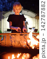 A cute boy is roasting sausages using skewers over a campfire on a summer evening. An active outdoor getaway for a family with children during a countryside vacation. Camping 142787882