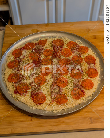 Unbaked pepperoni pizza on metal tray on cutting board 142788167