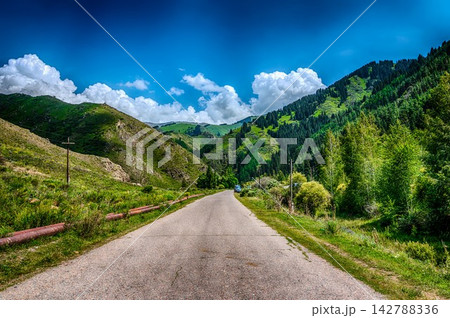 Paved mountain road winding through green hills under dramatic sky Kyrgyzstan Paved mountain road winding through green hills under dramatic sky Kyrgyzstan 142788336