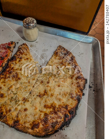 Thin crust pizza slices on baking tray with shaker 142788407
