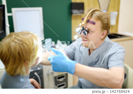 An experienced male ENT doctor examines a young patient's nose in a medical office. A professional otolaryngologist is at his workplace An experienced male ENT doctor examines a young patient's nose in a medical office. A professional otolaryngologist is at his workplace 142788924