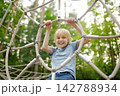 Cute preteen boy having fun with climbing frames on outdoor playground. Spring or summer or autumn active sport leisure for child. Outdoor activities for family with children. Equipment of 142788934