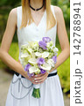 A slender caucasian bride in a stylish dress holds a wedding bouquet; the focus is on her hand and rings. An outdoor wedding photo session. 142788941