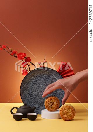 Cropped hand reaching for traditional mooncake for Mid Autumn Festival celebration Cropped hand reaching for traditional mooncake for Mid Autumn Festival celebration 142789715