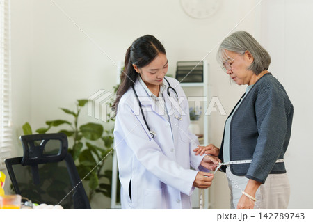 Asian doctor measuring senior woman waist size for health checkup and weight management 142789743