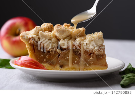 Apple crumble pie slice on a white plate with caramel sauce poured from a spoon 142790883