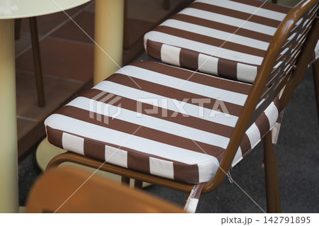 Chairs with striped cushions placed around a circular table outside Chairs with striped cushions placed around a circular table outside 142791895