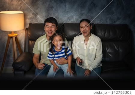 funny family (mother, father and daughter) laughing while watching comedy film on tv in the living room at night funny family (mother, father and daughter) laughing while watching comedy film on tv in the living room at night 142795305