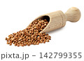 Raw buckwheat pouring from a wooden scoop close-up on a white background. Isolated 142799355