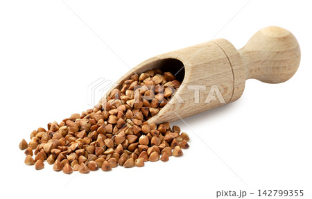 Raw buckwheat pouring from a wooden scoop close-up on a white background. Isolated Raw buckwheat pouring from a wooden scoop close-up on a white background. Isolated 142799355