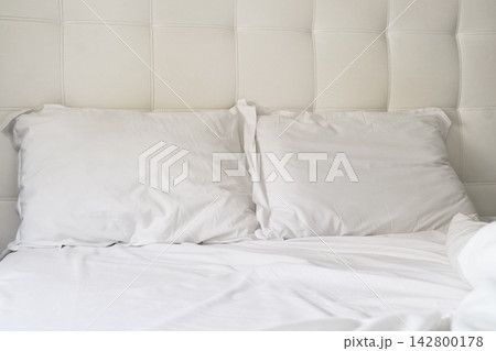 Bedding with two pillows on a clean white bed in a simple room setting during daylight hours Bedding with two pillows on a clean white bed in a simple room setting during daylight hours 142800178