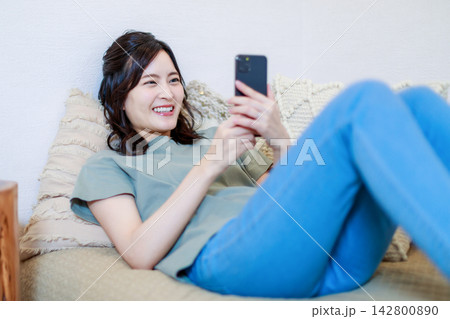 ソファーで寝ころんでスマホを使う女性 ソファーで寝ころんでスマホを使う女性 142800890