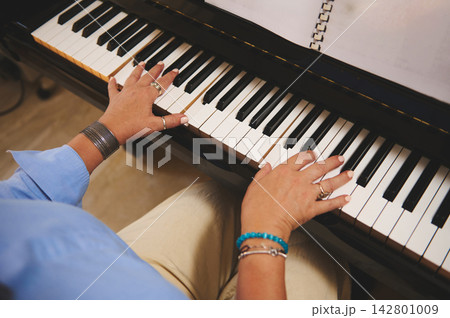 Woman playing piano with sheet music, hands on keys practicing a melody in close-up Woman playing piano with sheet music, hands on keys practicing a melody in close-up 142801009