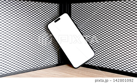 A mockup phone with a blank white screen leans diagonally in a wooden shelving corner. The template A mockup phone with a blank white screen leans diagonally in a wooden shelving corner. The template 142801092