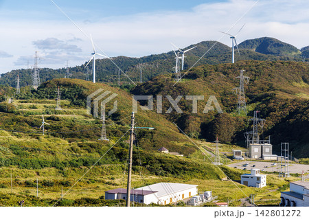 津軽半島の丘陵地帯に立ち並ぶ風力発電機と送電鉄塔 津軽半島の丘陵地帯に立ち並ぶ風力発電機と送電鉄塔 142801272
