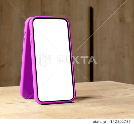Pair of smartphone mockups with blank white screens and magenta frames lean together on a wooden 142801787