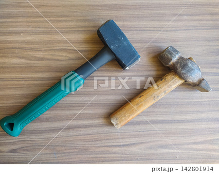 Two hammers, one modern with a vibrant green grip and one vintage with a weathered wooden handle, lie on a rustic wood surface, symbolizing the evolution of manual labor. Nobody. Two hammers, one modern with a vibrant green grip and one vintage with a weathered wooden handle, lie on a rustic wood surface, symbolizing the evolution of manual labor. Nobody. 142801914