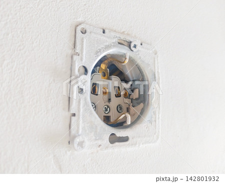 An unfinished electrical socket exposed on a white textured wall during a home renovation project. Nobody is present, evoking a raw feeling of DIY progress and potential danger. An unfinished electrical socket exposed on a white textured wall during a home renovation project. Nobody is present, evoking a raw feeling of DIY progress and potential danger. 142801932