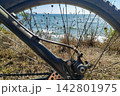 Framed by a bicycle wheel, a peaceful coastal view of the blue sea evokes feelings of freedom, active adventure, and serene summer exploration on a sunny day. There are no people. 142801975