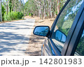 A closeup of a blue cars side mirror reflecting the sky on a sunny forest road trip, evoking a powerful sense of freedom, peaceful adventure, and escape. There are no people. 142801983