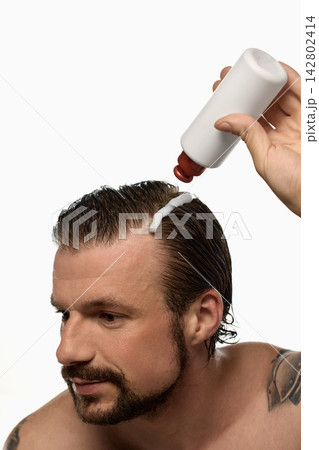 Bearded man dispensing liquid product directly onto wet hair 142802414