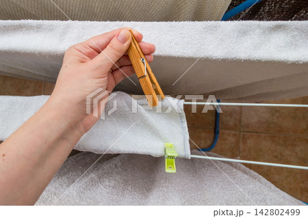 Hand putting wooden clothespin on white towel drying on a clothesline Hand putting wooden clothespin on white towel drying on a clothesline 142802499