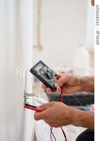 Electrician testing wall socket voltage with digital multimeter Electrician testing wall socket voltage with digital multimeter 142804820