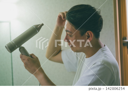 脱衣所でドライヤーと手ぐしで丁寧に髪を整えるアラフォー男性 脱衣所でドライヤーと手ぐしで丁寧に髪を整えるアラフォー男性 142806254