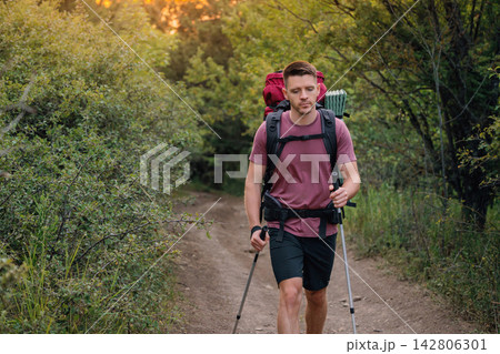 Handsome man trekking through woods path with backpack and poles Handsome man trekking through woods path with backpack and poles 142806301
