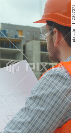 Vertical video. Close-up portrait of engineer with blueprint in front of building under construction. Vertical video. Close-up portrait of engineer with blueprint in front of building under construction. 142807073