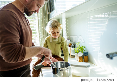 Dad and toddler preparing simple meal together in bright kitchen. Dad and toddler preparing simple meal together in bright kitchen. 142807204