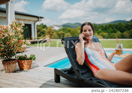 Young woman in swimsuit sitting by pool, making phone call. 142807286