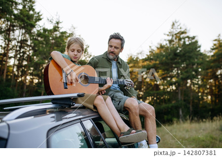 Dad teaching boy how to play guitar during summer camping adventure in nature. Dad teaching boy how to play guitar during summer camping adventure in nature. 142807381
