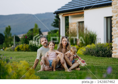 Family enjoying late summer evening together at their new house, sitting on grass. Family enjoying late summer evening together at their new house, sitting on grass. 142807462
