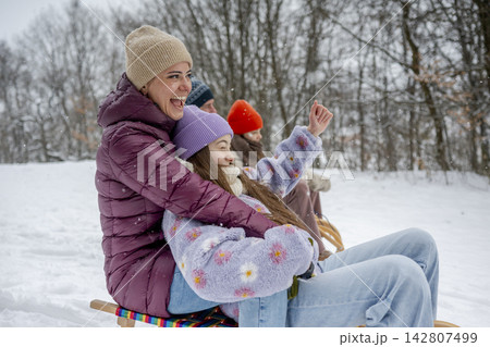 Family enjoying winter sledding together on snowy hill. 142807499
