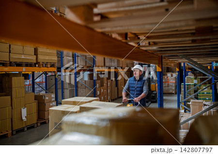 Older male warehouse worker pulling a pallet truck. 142807797