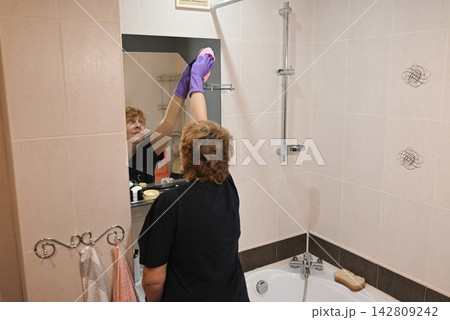 Woman cleaning bathtub in bathroom during afternoon 142809242