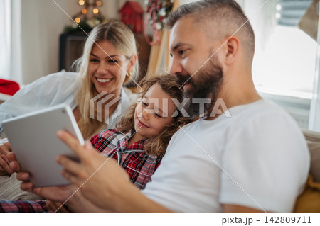 Family watching Christmas movie together on tablet during cozy holiday at home. Family watching Christmas movie together on tablet during cozy holiday at home. 142809711