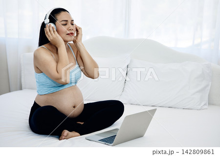 Pregnant woman wearing headphones and listening to music with laptop on bed at home, enjoying calm relaxation, maternity wellness and peaceful digital entertainment Pregnant woman wearing headphones and listening to music with laptop on bed at home, enjoying calm relaxation, maternity wellness and peaceful digital entertainment 142809861