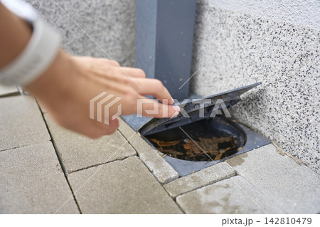 Person opens outdoor drain cover with leaves and debris inside 142810479