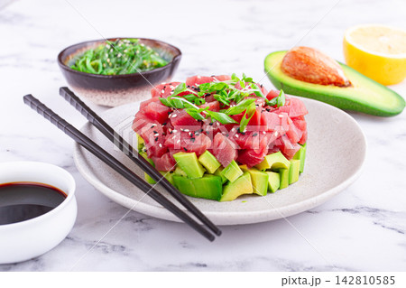 Fresh tuna tartare with avocado served on a marble table with soy sauce and seaweed salad 142810585