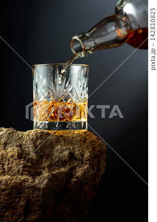 Whiskey is poured from a bottle into a glass. Whiskey is poured from a bottle into a glass. 142810825