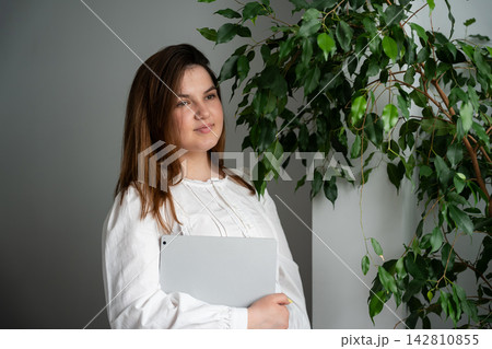 Female freelancer holding a tablet beside a leafy houseplant in a bright home interior. Remote work personal branding and freelance career Female freelancer holding a tablet beside a leafy houseplant in a bright home interior. Remote work personal branding and freelance career 142810855