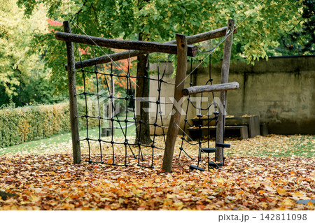 Wooden rope climbing frame stands on fallen leaves in an autumn playground. Concept of childhood, recreation, play, outdoor activity and movement 142811098