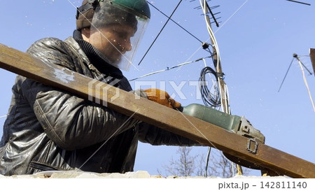 Young mechanic in protective gloves polishing iron using electric grinder wheel at construction. Professional repairman grinding metal details with circular saw on house at sunny day. Slow mo Young mechanic in protective gloves polishing iron using electric grinder wheel at construction. Professional repairman grinding metal details with circular saw on house at sunny day. Slow mo 142811140