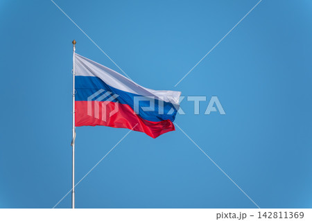 Russian tricolor flag waving in the wind against a blue sky. Fieldbird sits on a branch in spring with a blurred background. Russian tricolor flag waving in the wind against a blue sky. Fieldbird sits on a branch in spring with a blurred background. 142811369